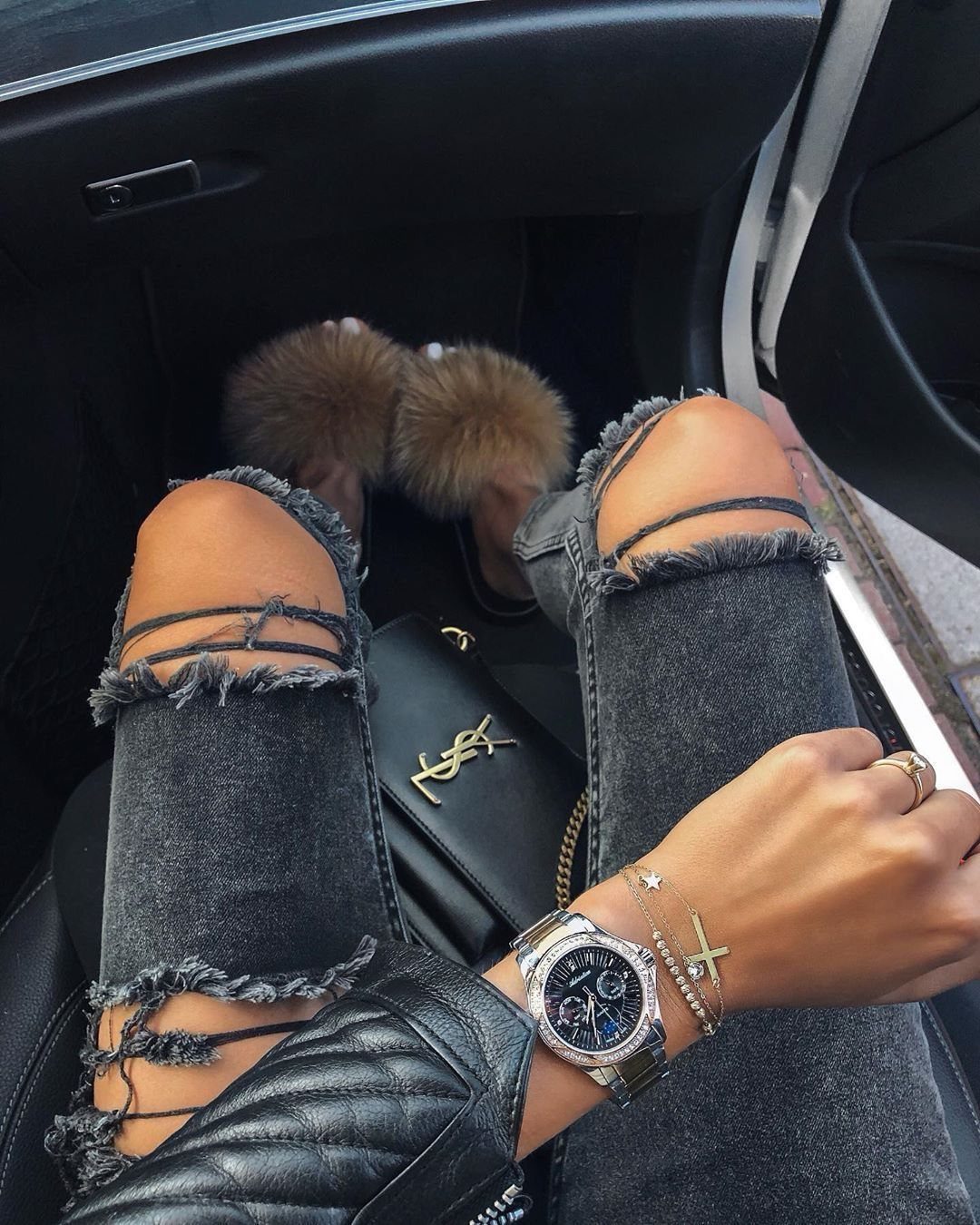 Person wearing ripped grey denim jeans and a sparkling silver watch while sitting in a car.
