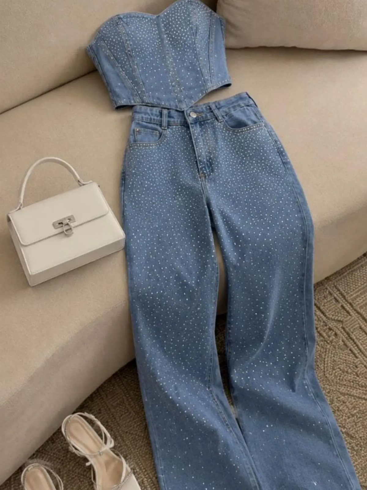 Rhinestone embellished denim corset top and matching wide-leg pants laid on a beige sofa.