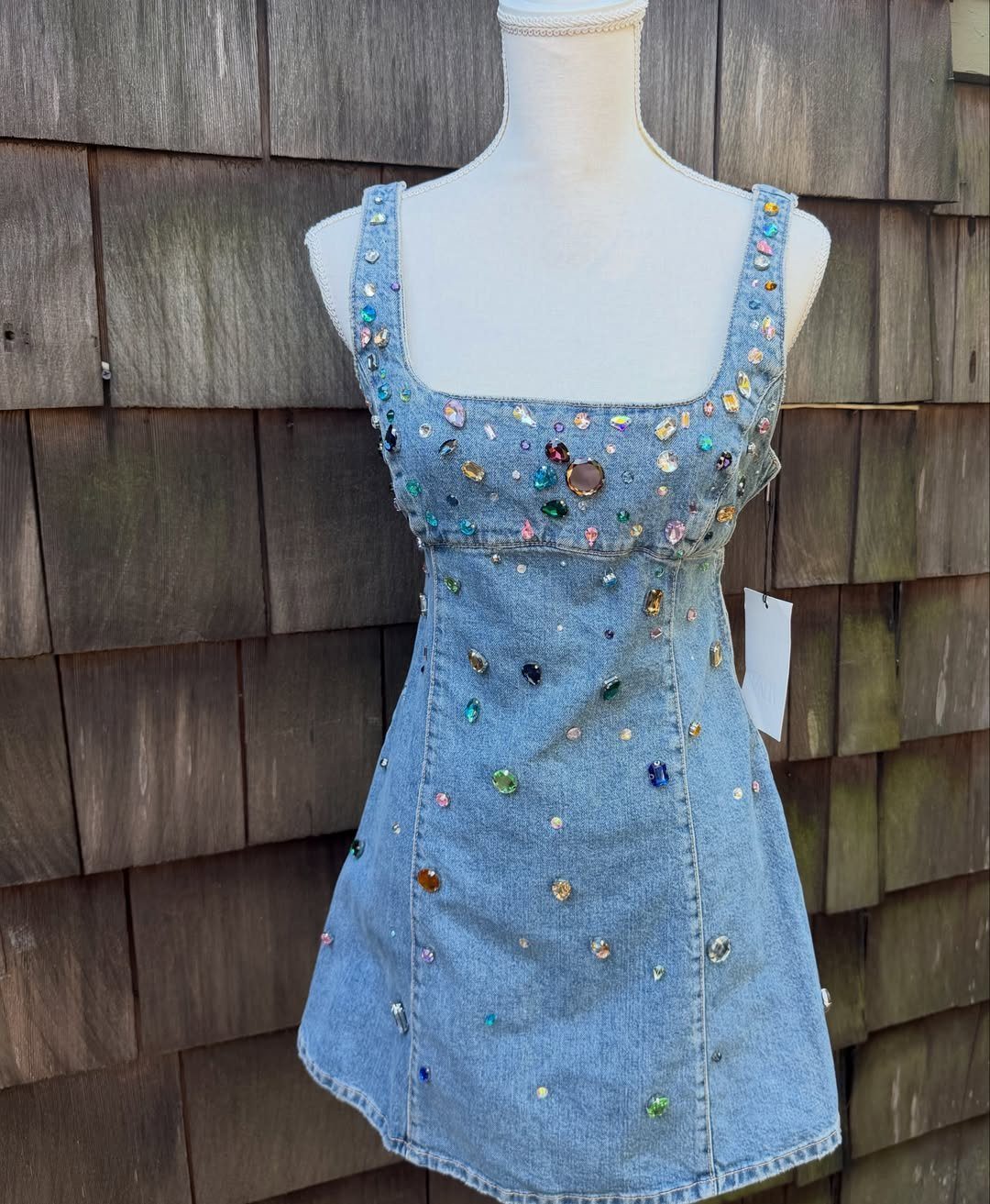 A light wash denim mini dress decorated with colorful rhinestones on a white mannequin.