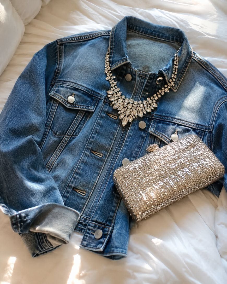 A blue denim jacket with a rhinestone necklace and a silver sequined clutch purse.