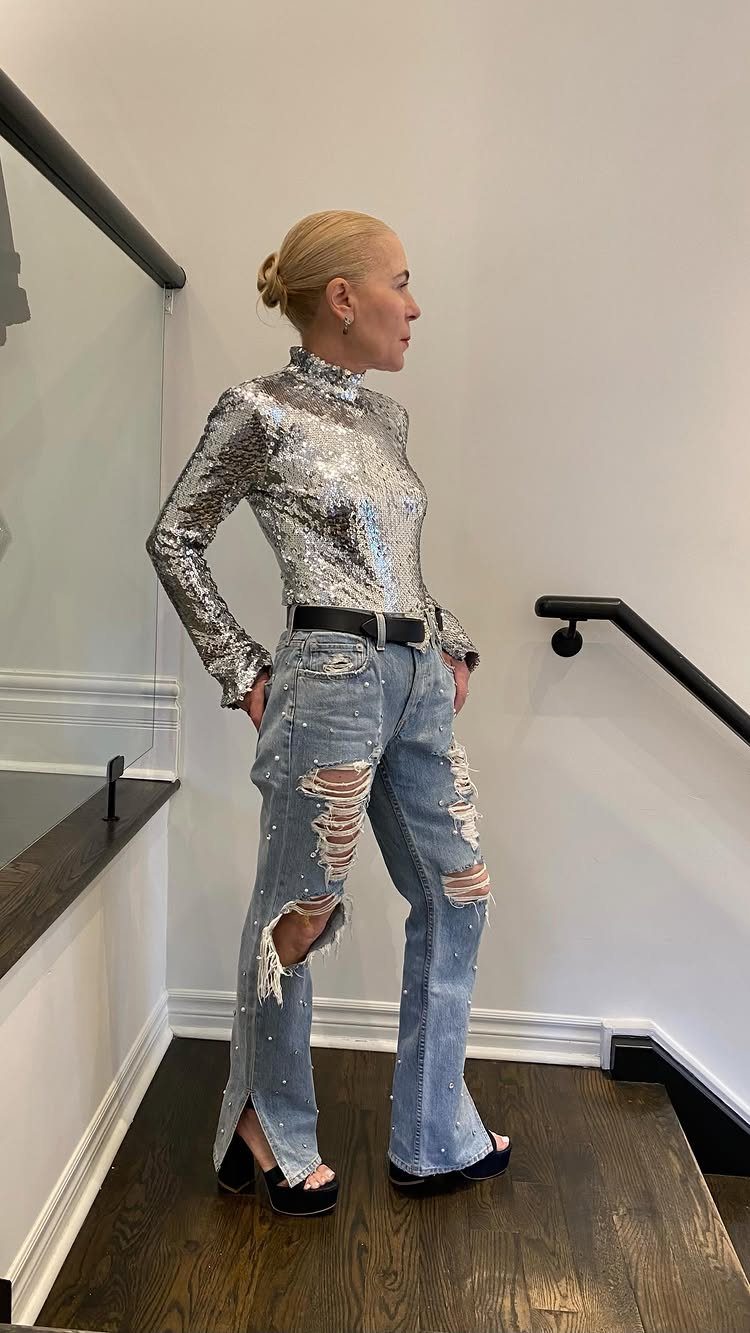 Woman wearing a silver sequined turtleneck and distressed light wash denim flare jeans.