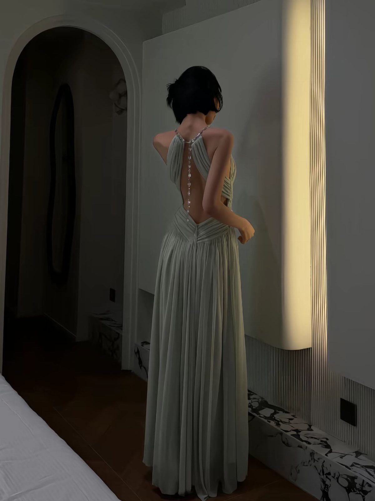Woman in a long, light-colored halter dress with a deep open back and pearl accents.