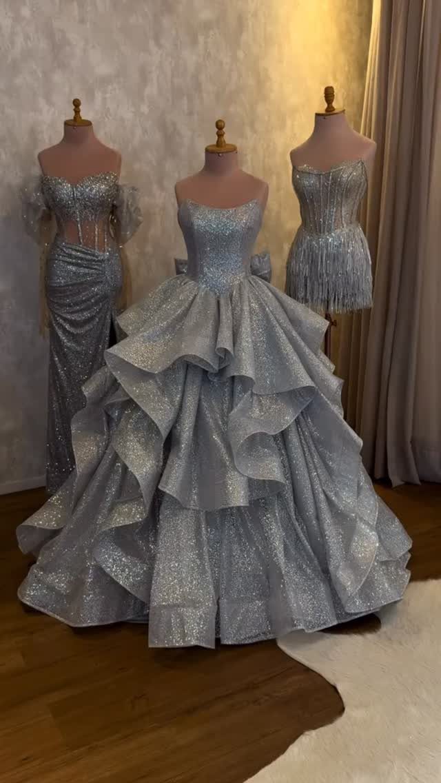 Three shimmering silver formal dresses displayed on mannequins in a room.