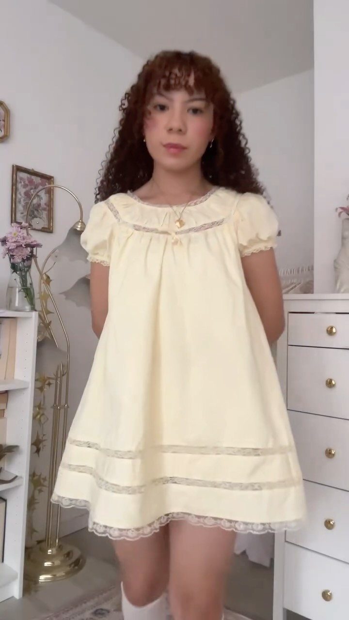 A young woman wearing a short, pale yellow babydoll dress with lace trim details.