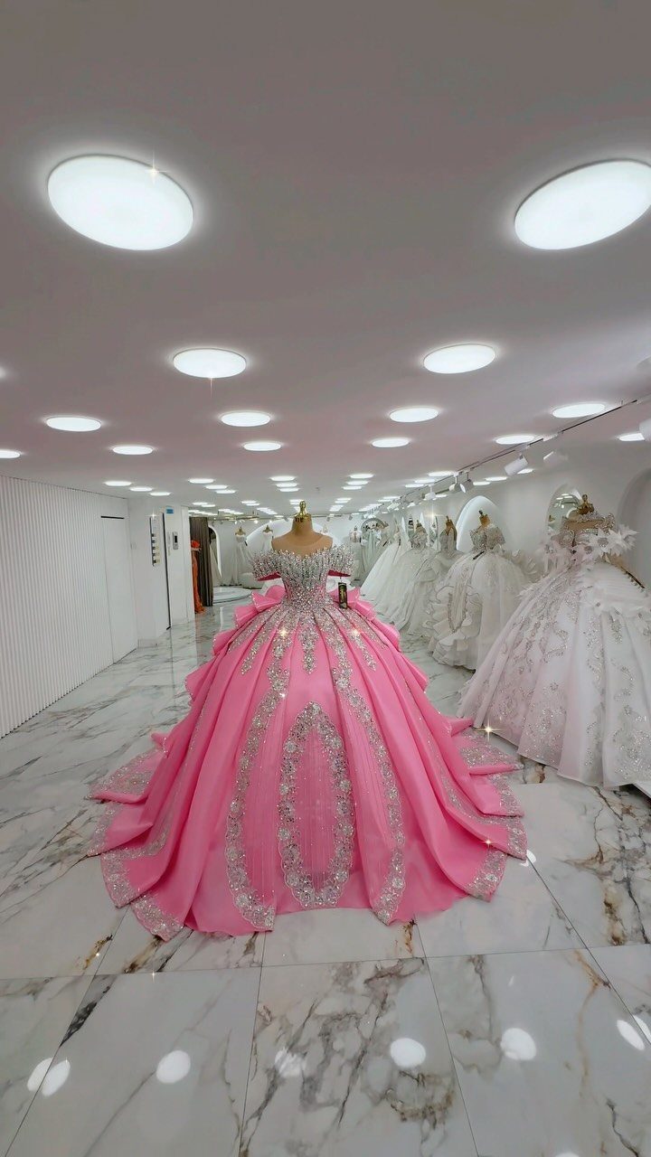 A voluminous pink ball gown with silver embroidery displayed on a mannequin in a bright showroom.