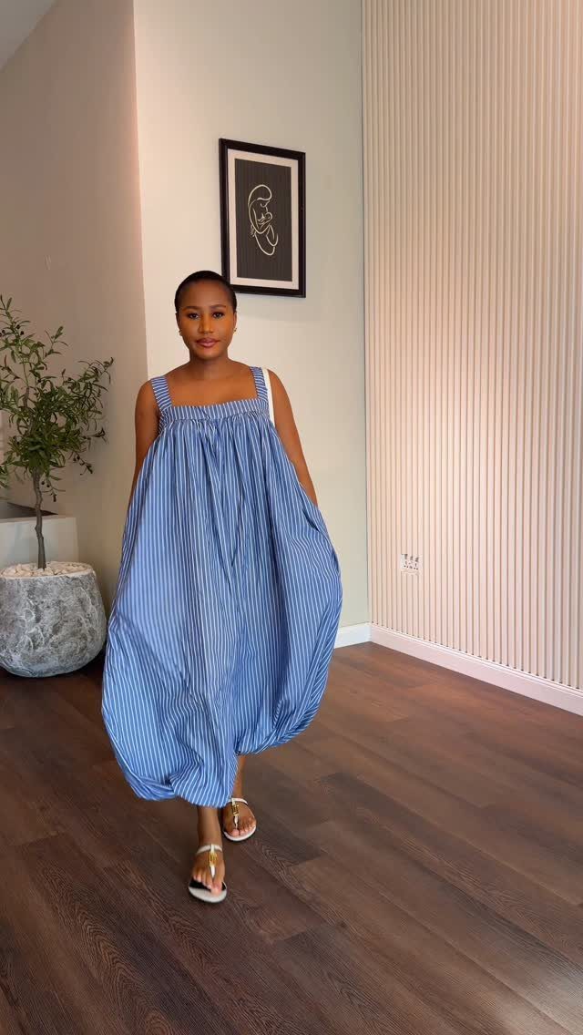 A woman wearing a voluminous blue and white striped balloon dress standing indoors.