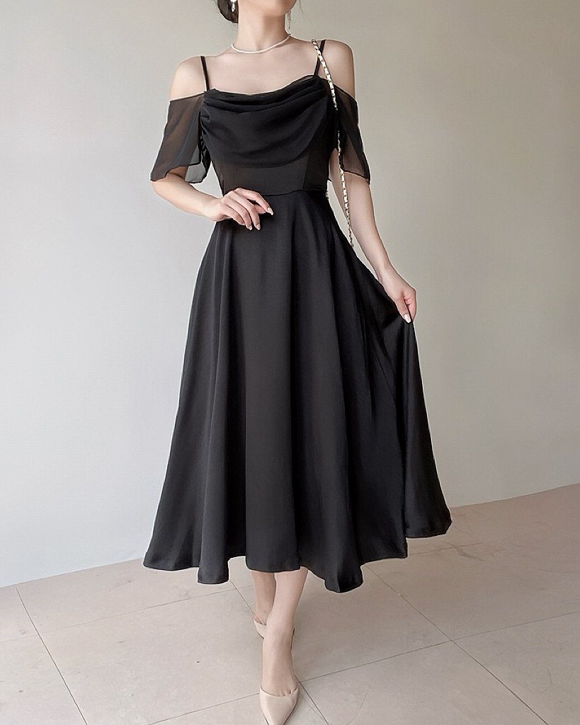 A person wearing a black midi dress with sheer sleeves and a cowl neckline.