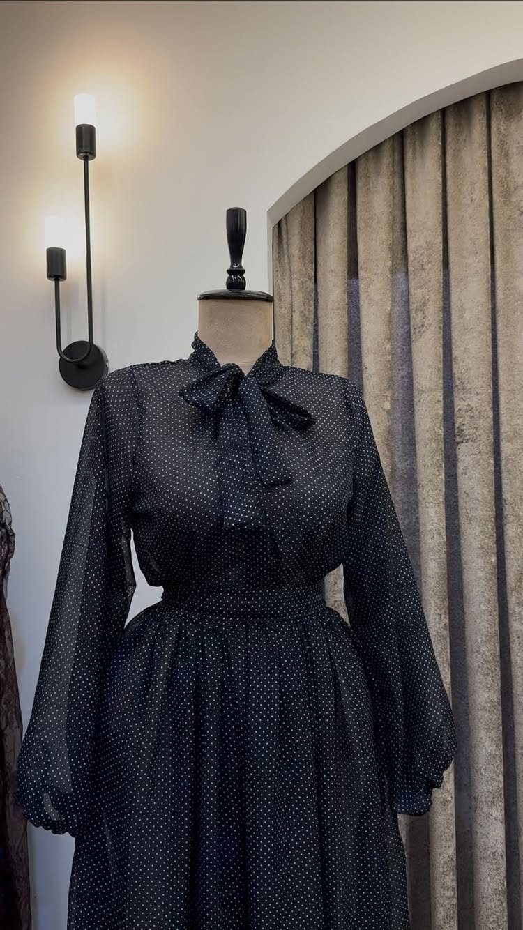 Black polka-dot dress with long sleeves and a large bow at the neck on a mannequin.