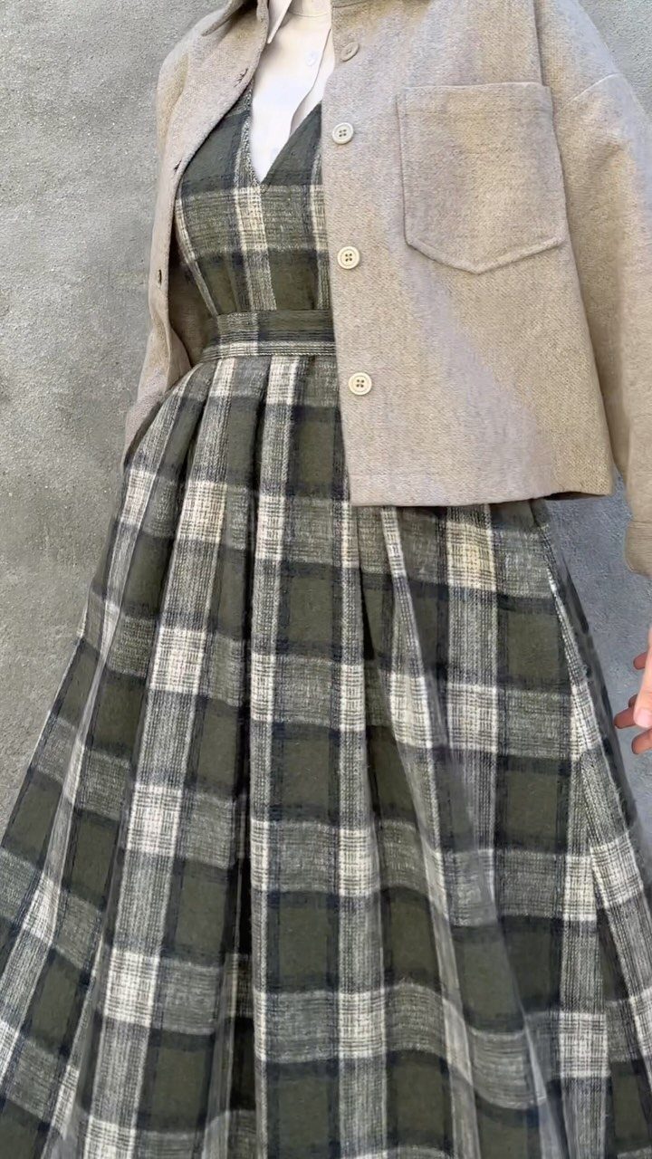A person wearing a green plaid jumper dress layered with a beige jacket.