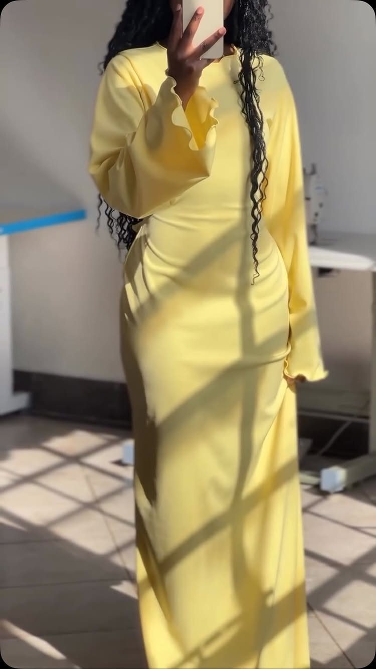 A person wearing a long yellow maxi dress with ruffled sleeves standing in sunlight.