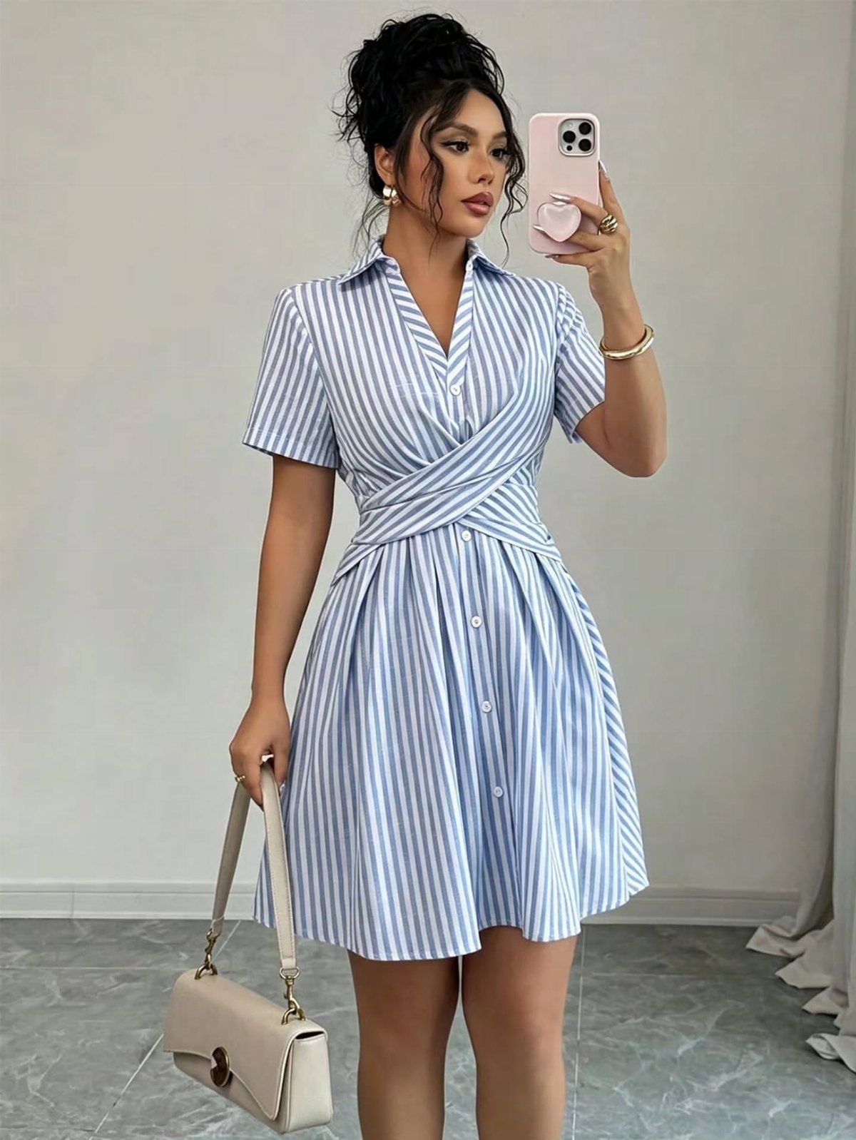 A woman in a blue and white striped shirt dress posing for a mirror selfie.