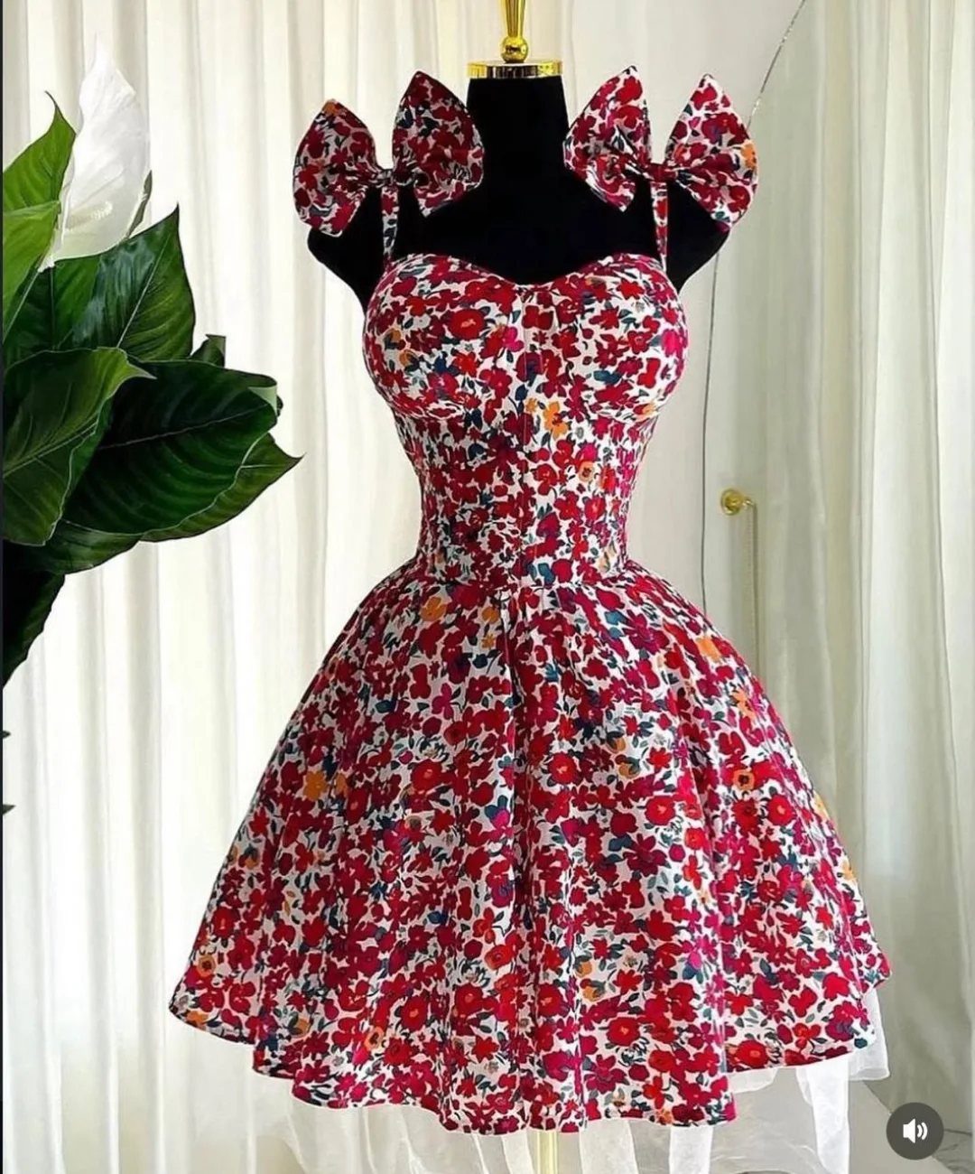 A red and white floral sundress with large bow straps displayed on a black mannequin.