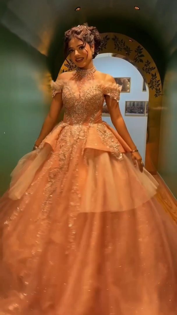 A woman wearing a voluminous peach-colored ball gown with an embellished bodice and layered tulle skirt.