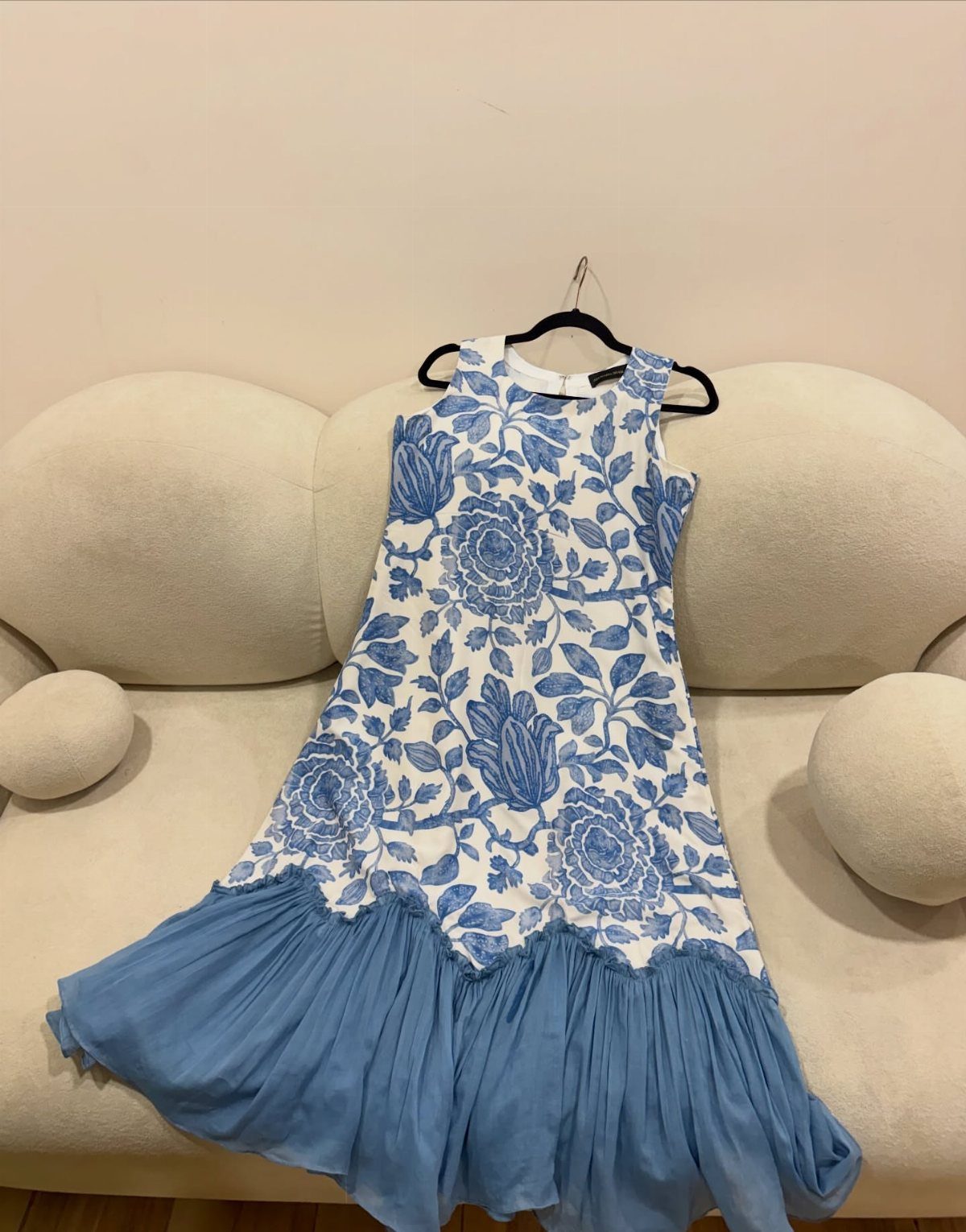 A blue and white floral sleeveless dress with a pleated hem hanging on a sofa.
