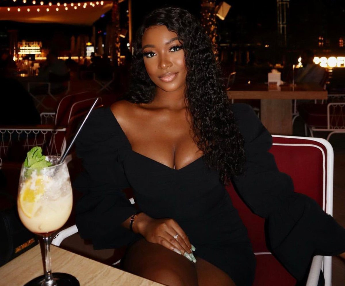 A woman with long curly hair wearing a black off-the-shoulder dress at an outdoor restaurant.