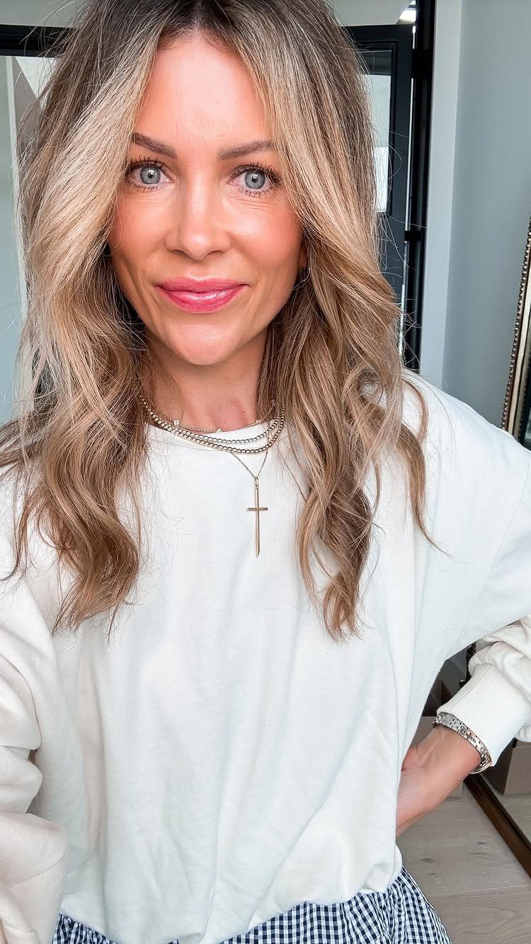 A smiling woman with blonde hair wearing layered silver necklaces with a cross pendant.
