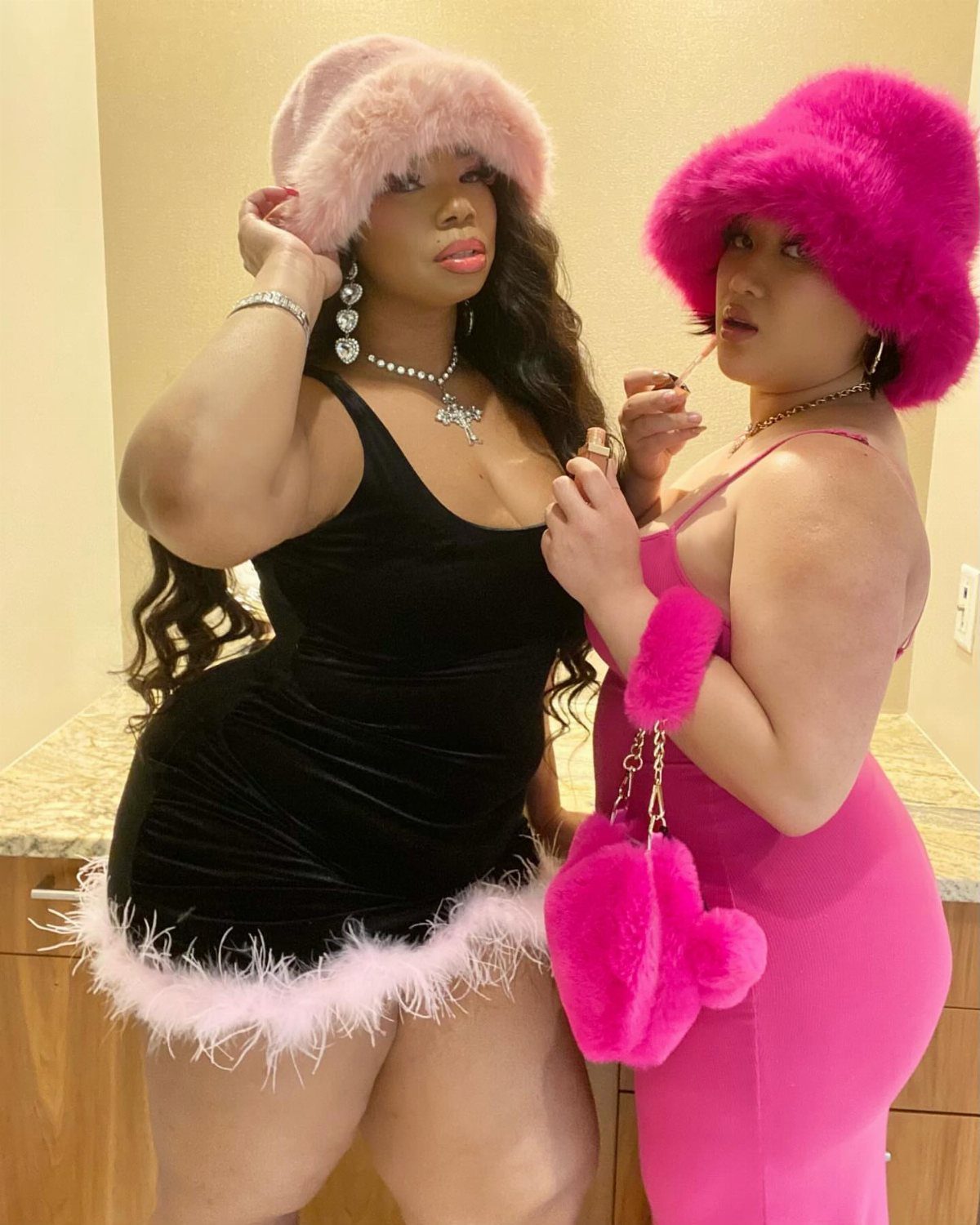Two women posing while wearing large, fuzzy pink bucket hats and colorful outfits.