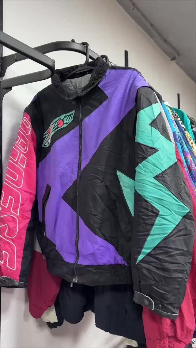 A colorful 90s style windbreaker with purple, teal, and pink geometric patterns hanging on a rack.