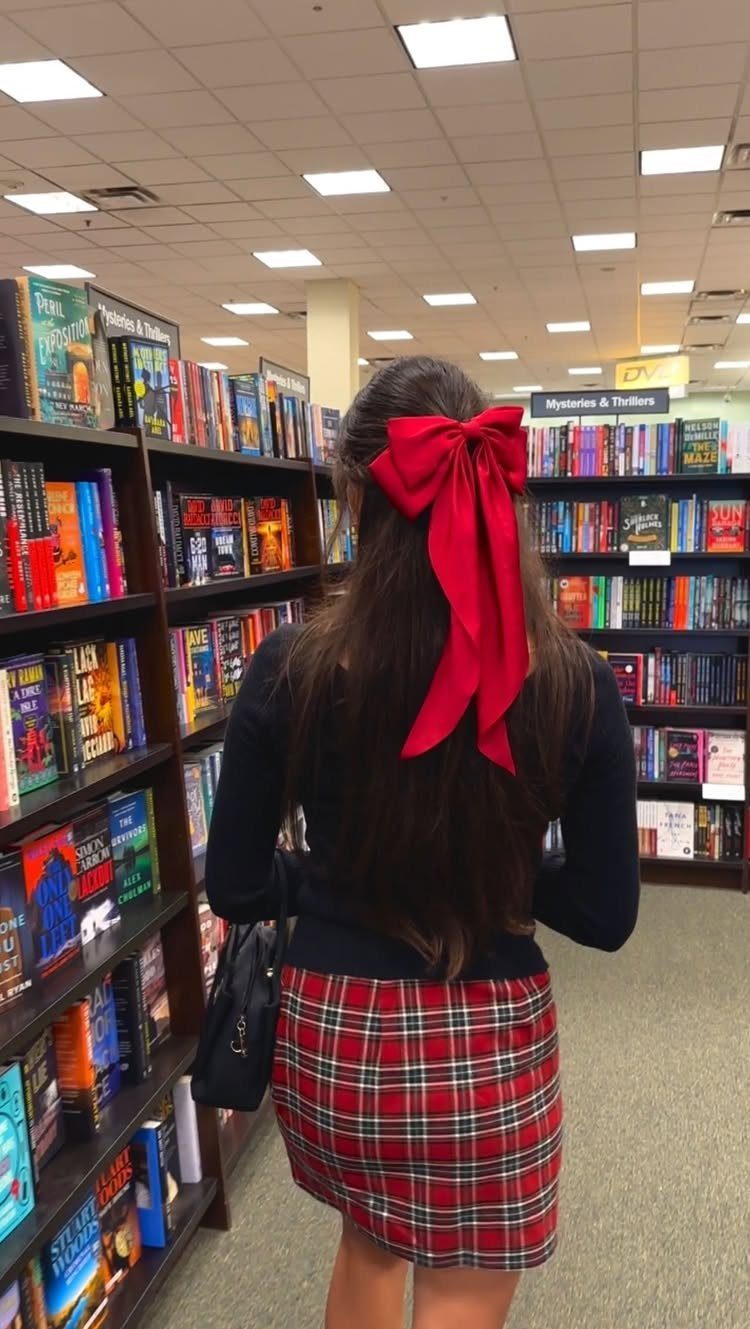 A person wearing a red plaid skirt and a large red hair bow in a bookstore.
