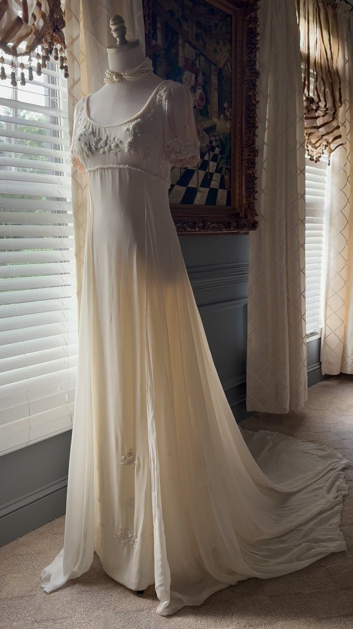 An ivory empire waist vintage gown displayed on a mannequin near a window.