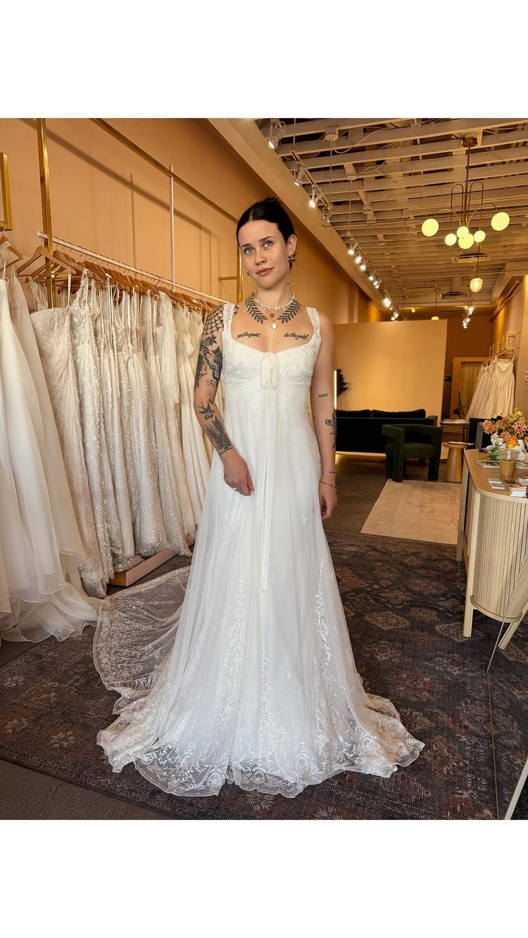 A woman wearing a white lace wedding dress standing in a bridal boutique.