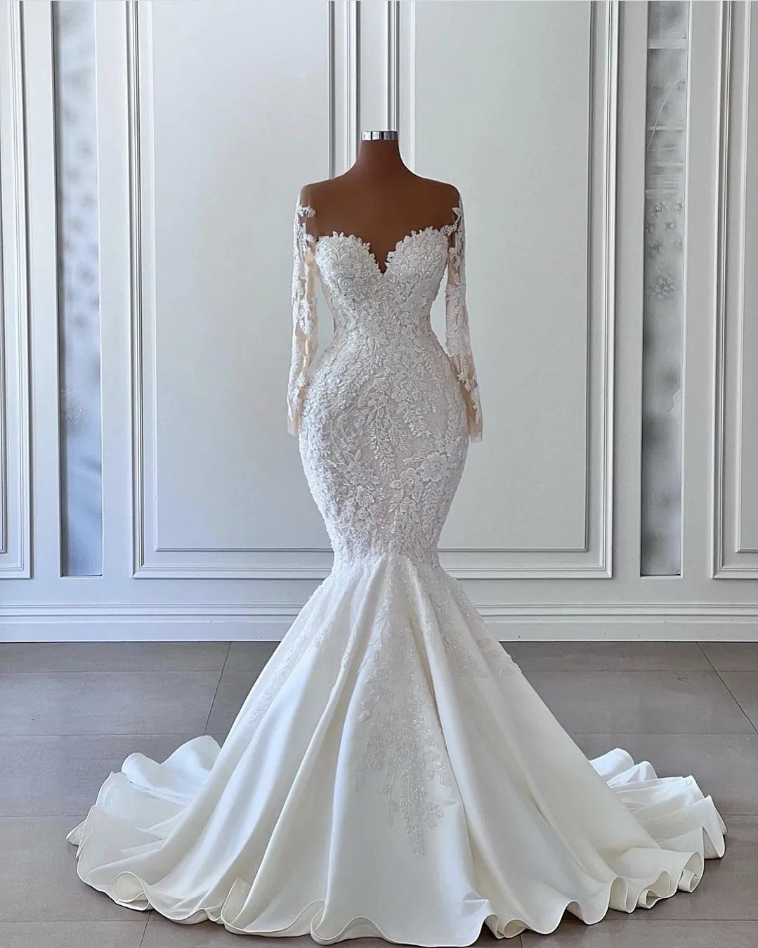 A white lace mermaid wedding dress with a long train displayed on a mannequin.