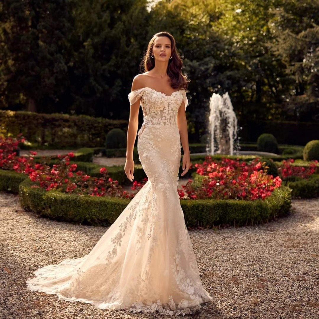 Woman wearing a lace off-the-shoulder trumpet silhouette wedding dress in a garden.