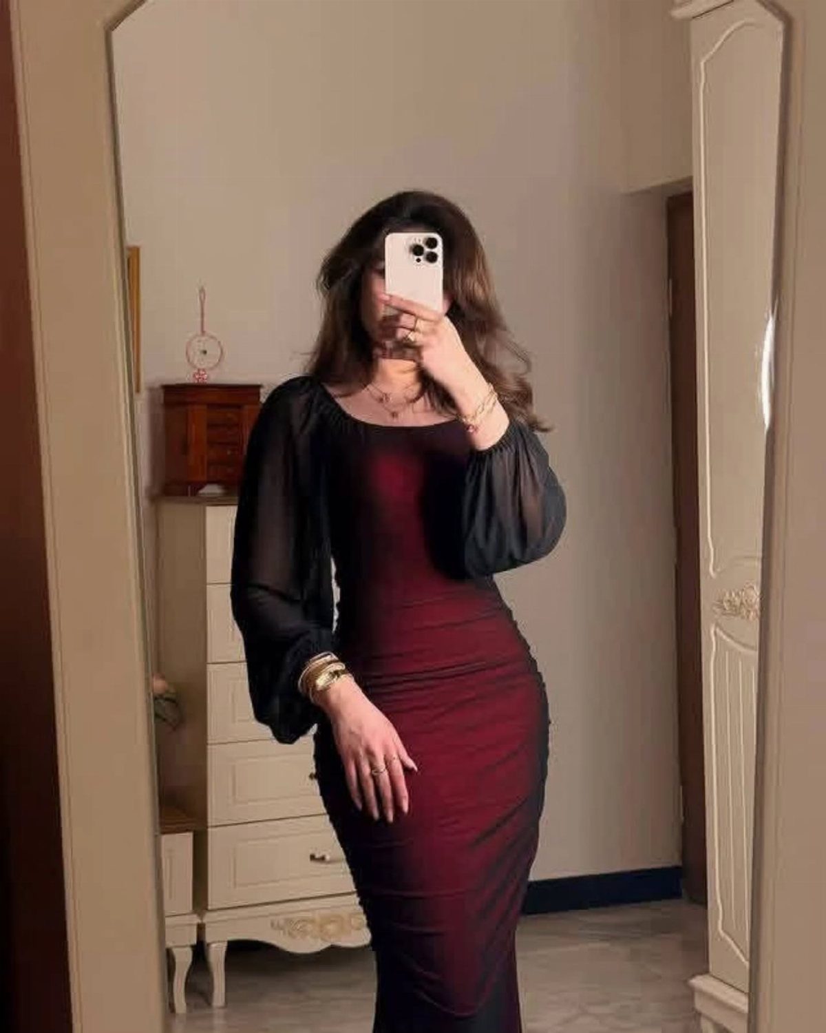 Woman in a dark red and black long-sleeved bodycon dress taking a mirror selfie.