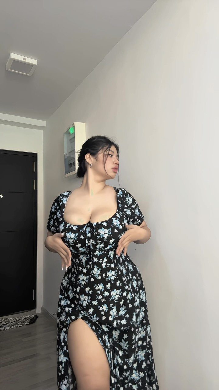 A woman wearing a black floral print dress with a sweetheart neckline standing against a white wall.