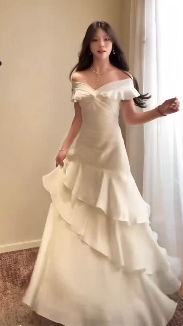 A woman posing in a white off-the-shoulder tiered mermaid gown indoors.