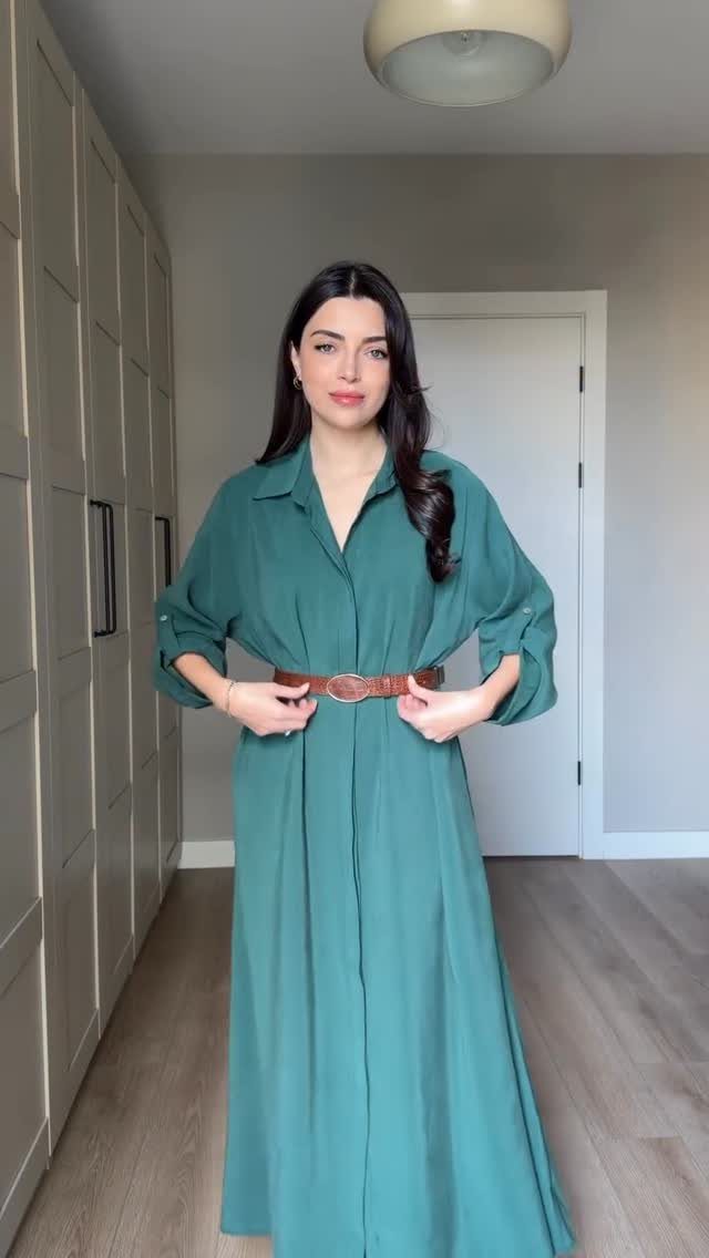 A woman wearing a long teal green shirt dress cinched with a brown leather belt.