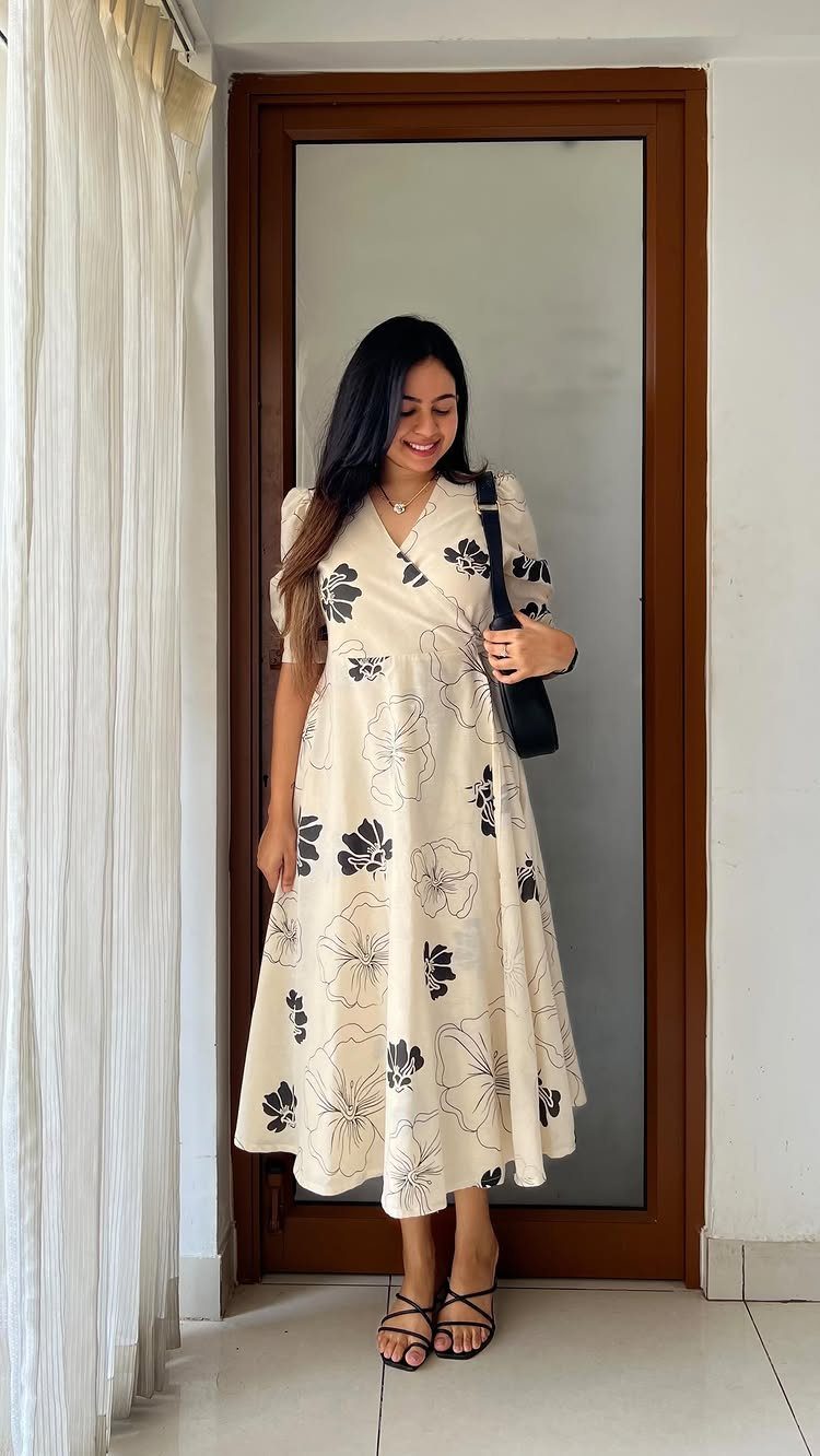 A woman wearing a cream and black floral wrap dress and black sandals.