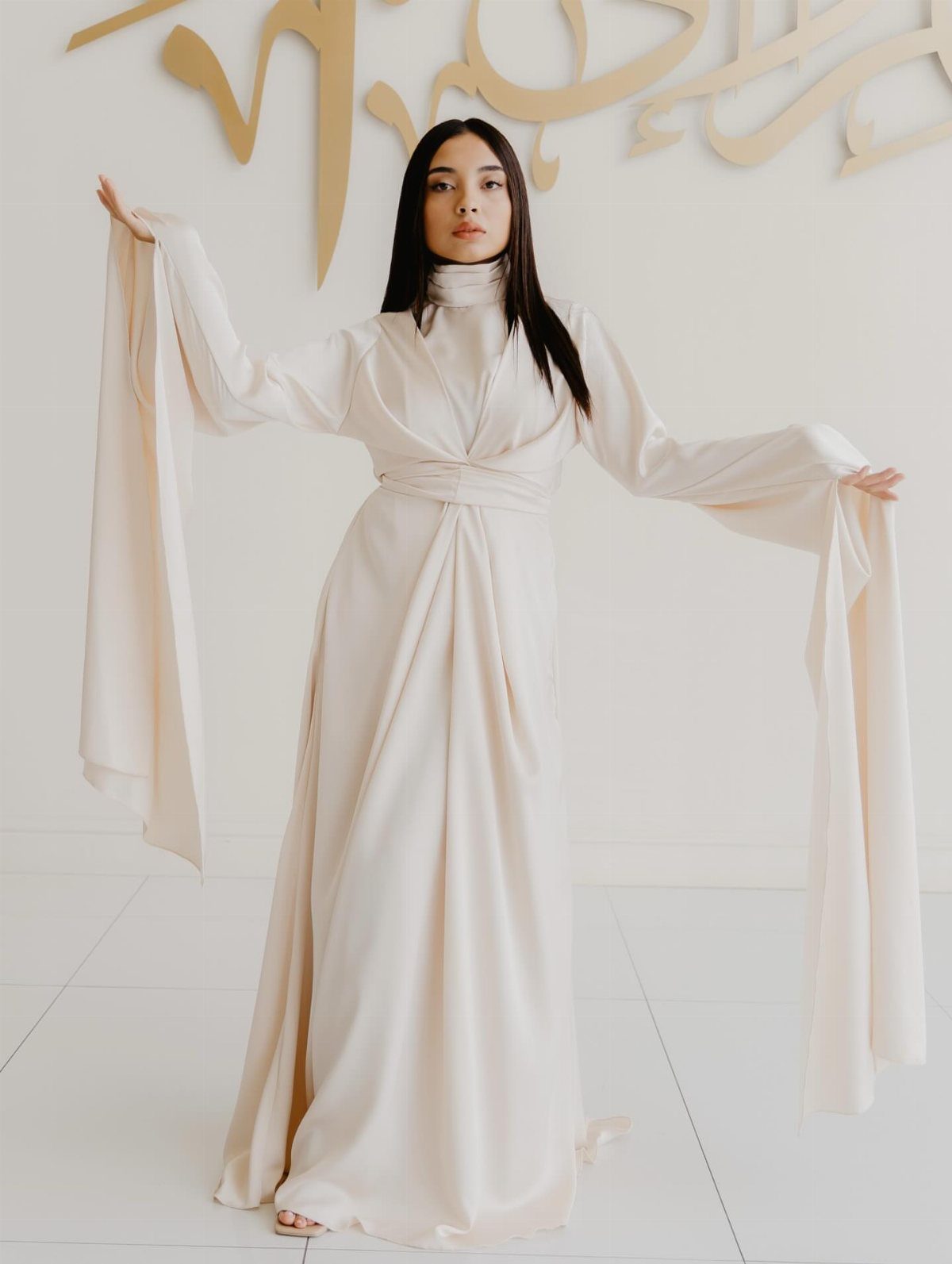 A woman wearing a cream satin dress with long, flowing shawl-like sleeves.