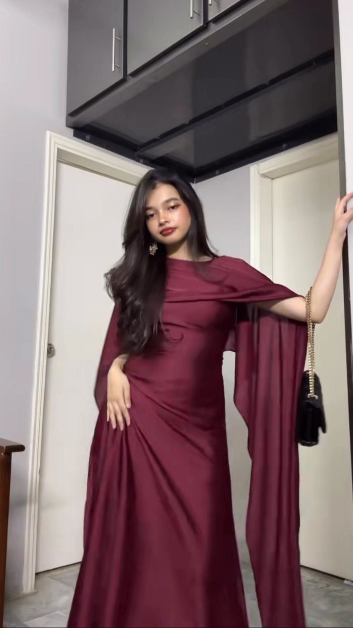 Woman in a maroon satin gown with a matching fabric cape draped over her shoulders.