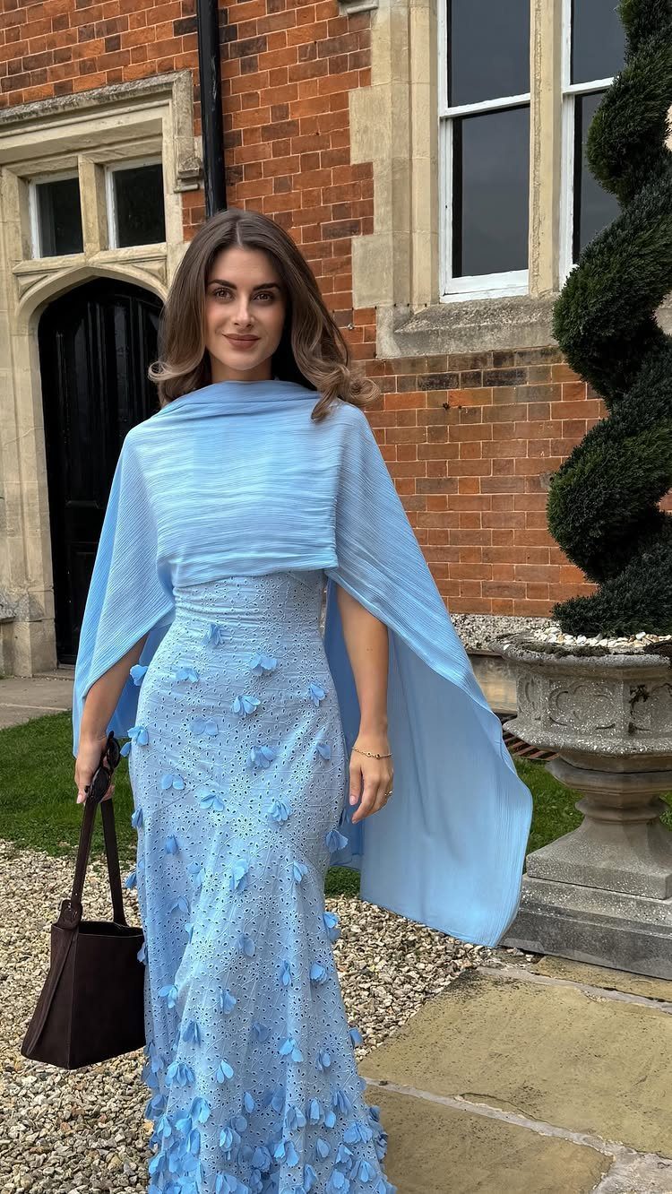 A woman wearing a light blue floral dress and a matching shawl standing outdoors.