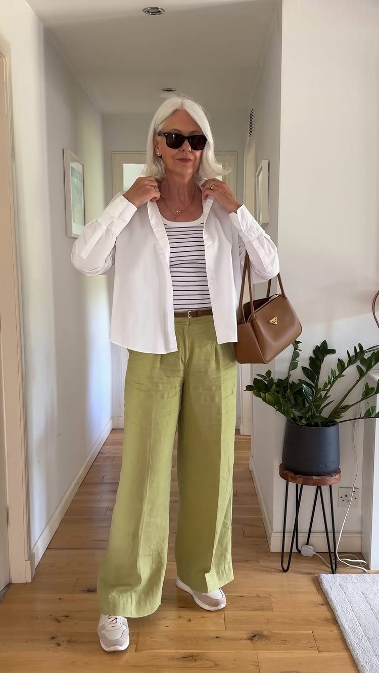 A woman with white hair wearing a white shirt, striped top, and green trousers.