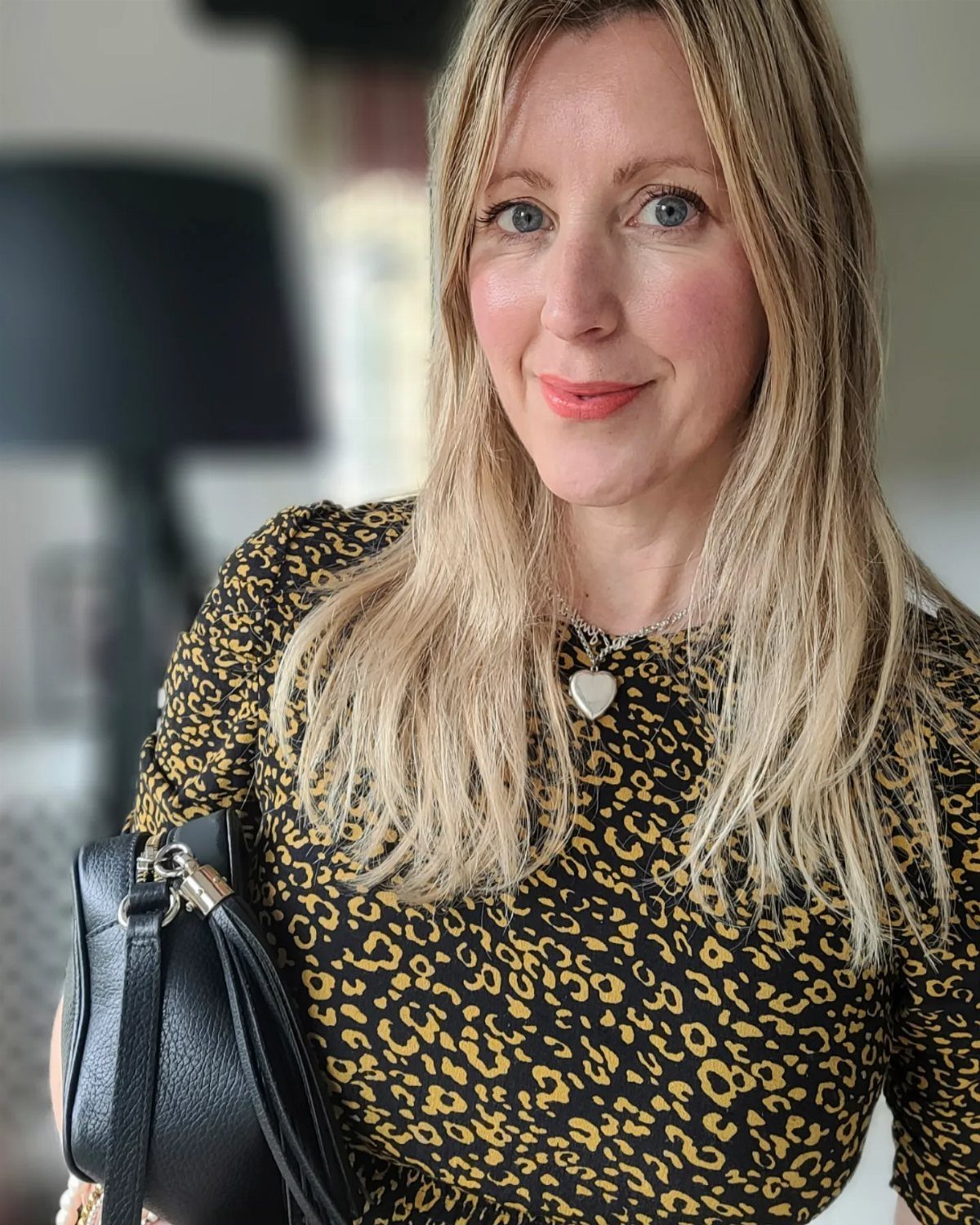 A blonde woman wearing a leopard print top and a heart necklace smiling at the camera.