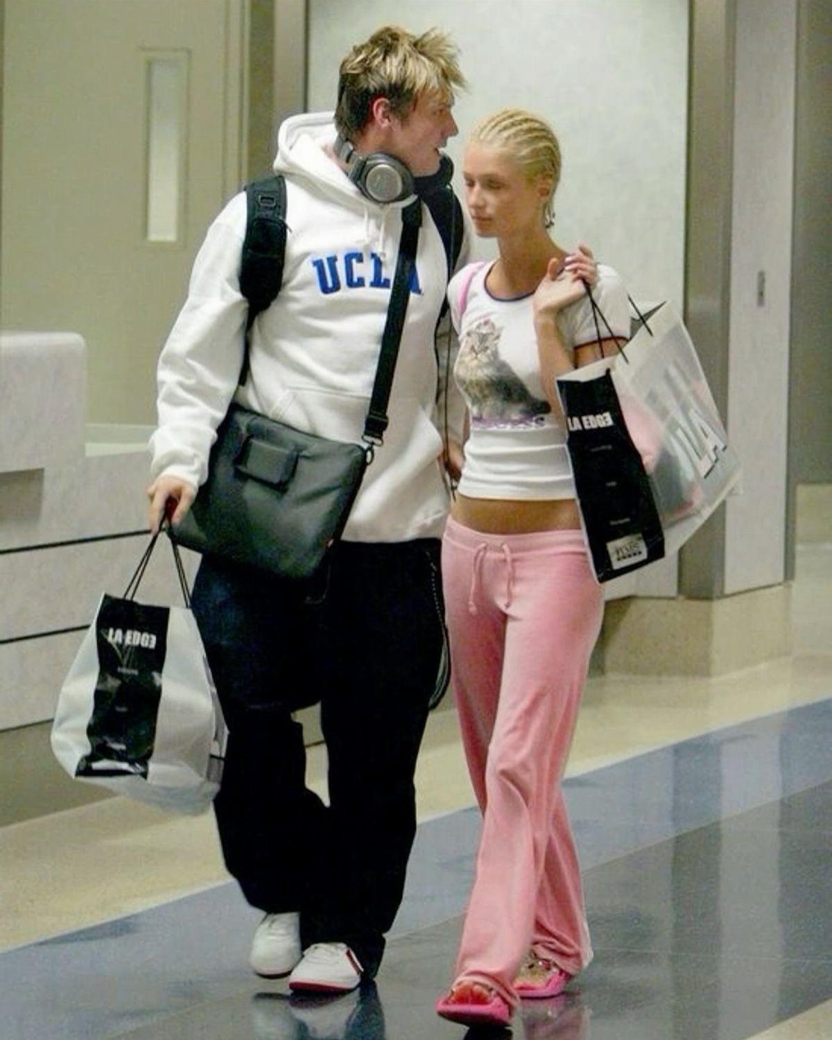 A man and woman walking through an airport carrying several shopping bags.