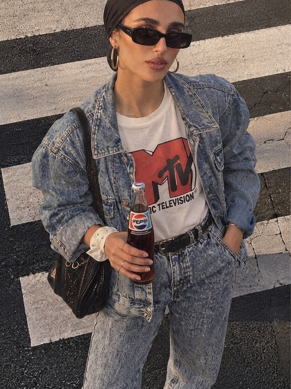 Woman in denim jacket and acid-wash jeans holding a Pepsi bottle on a crosswalk.