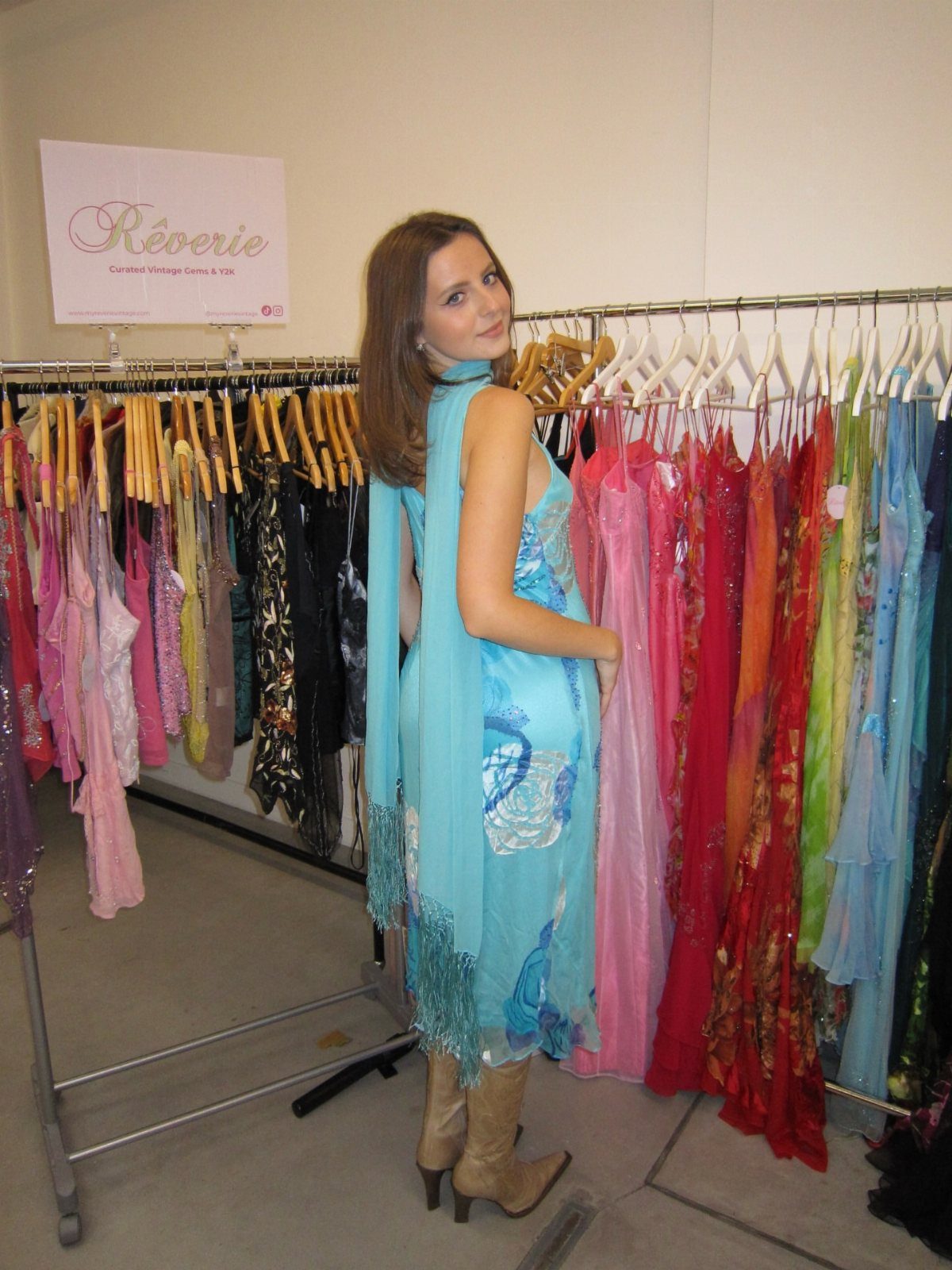 A woman posing in a light blue flowy dress standing in front of a clothing rack.