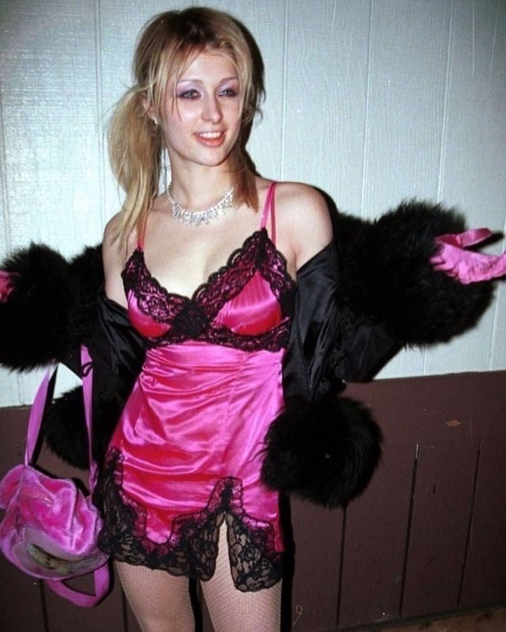 Blonde woman wearing a pink satin lace slip dress and a black faux fur jacket.