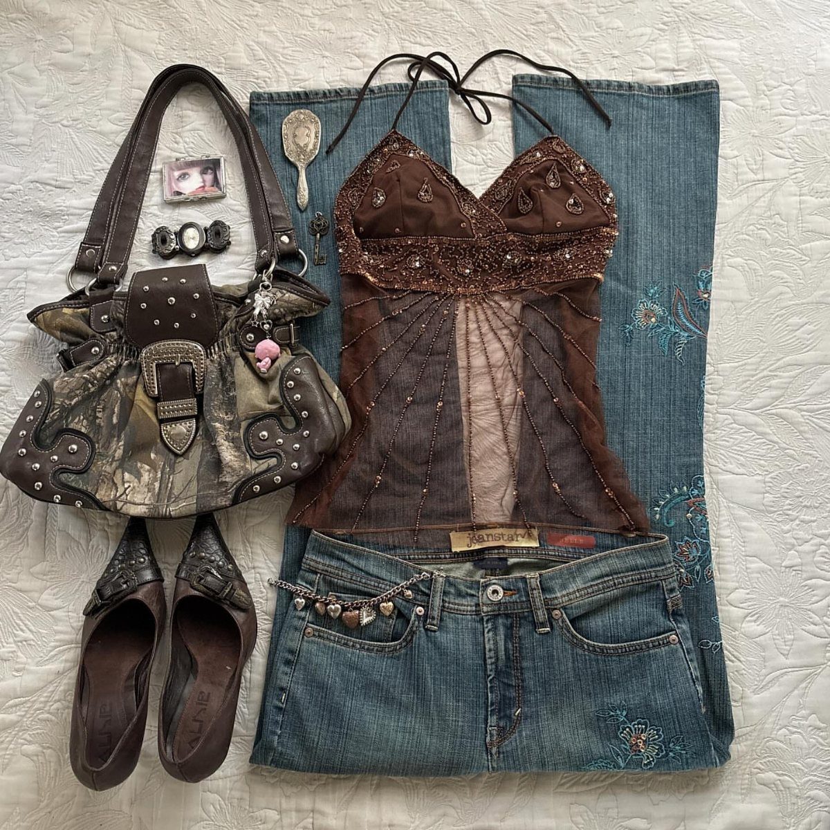 A brown sequined halter top laid over blue embroidered low-rise jeans with a patterned handbag.