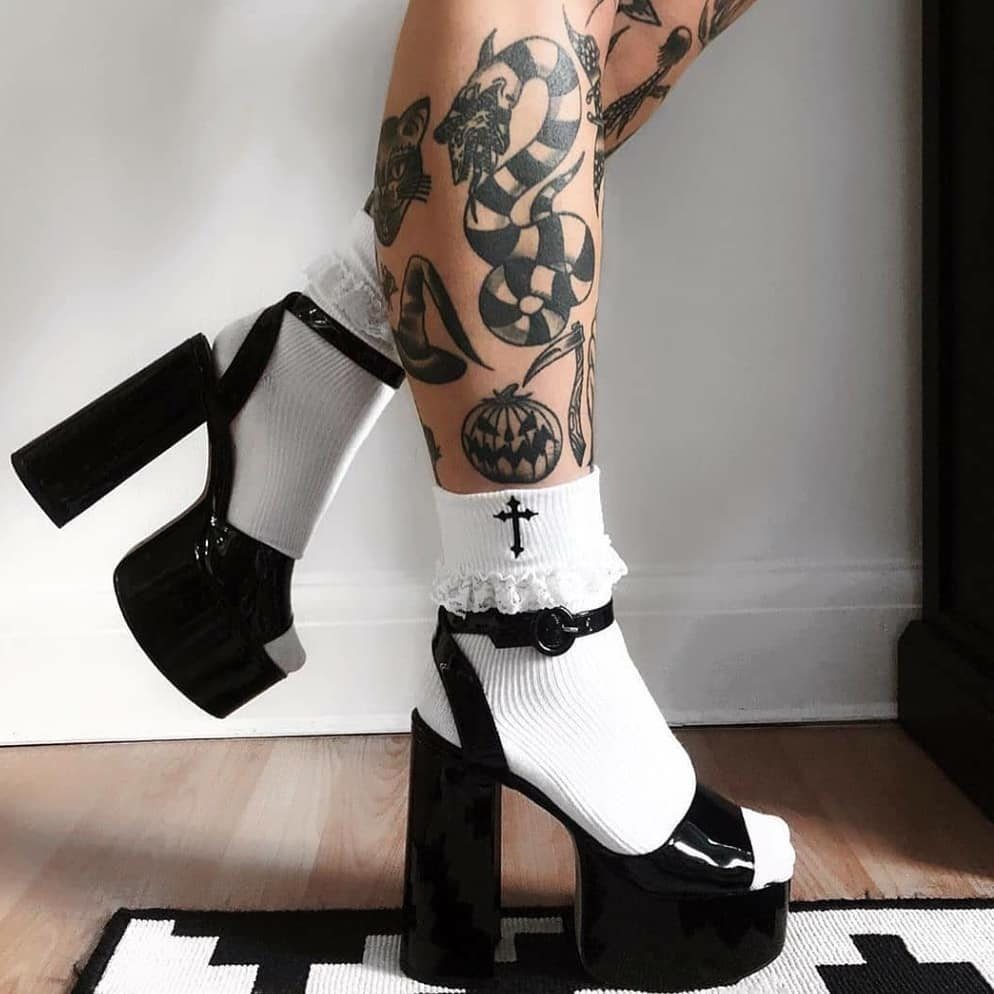 Tattooed legs wearing white ruffled socks and black patent leather platform sandals.
