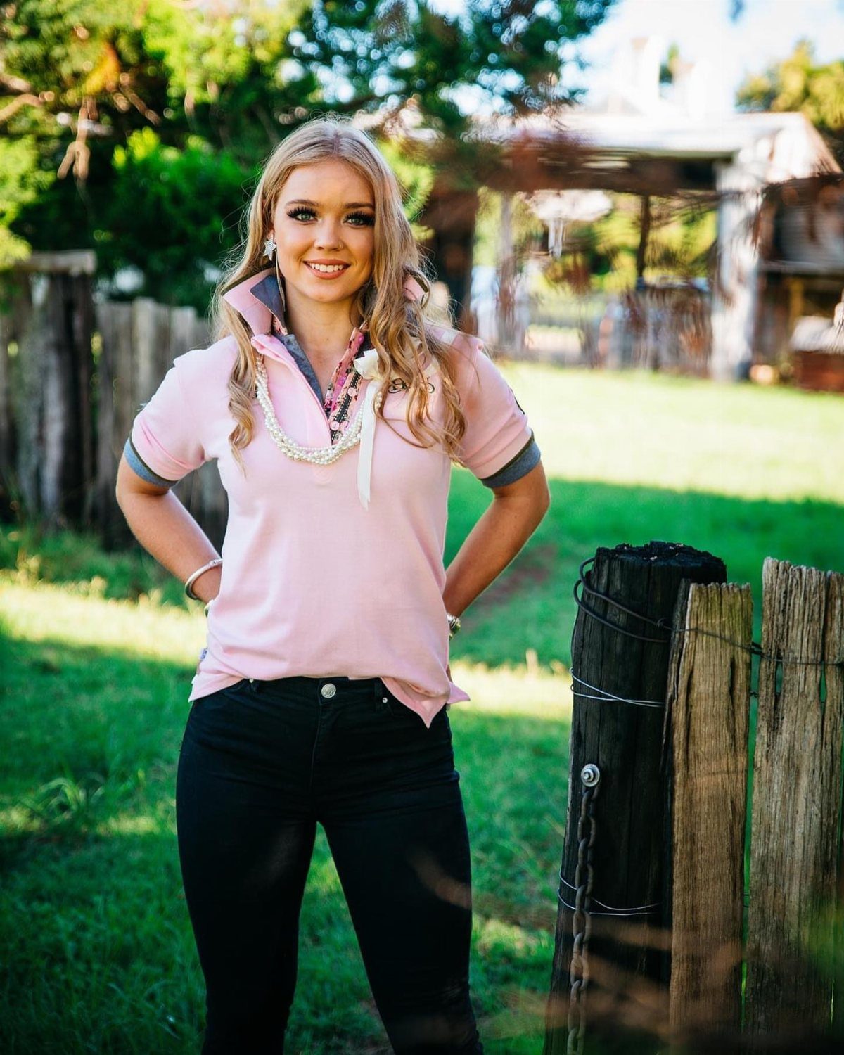 A blonde woman wearing a pink polo shirt with a popped collar standing in a field.