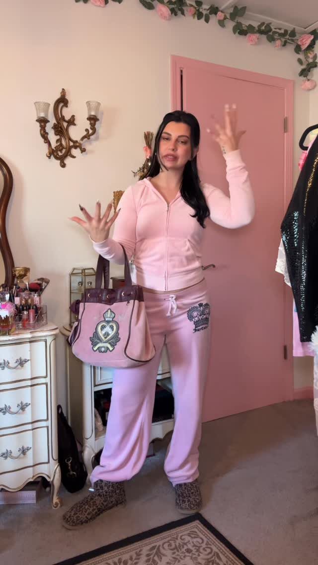 A woman posing in a pink velour tracksuit while holding a matching pink handbag.
