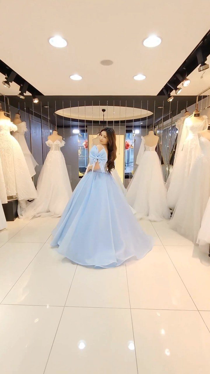 Woman wearing a voluminous light blue ball gown in a bridal boutique setting.