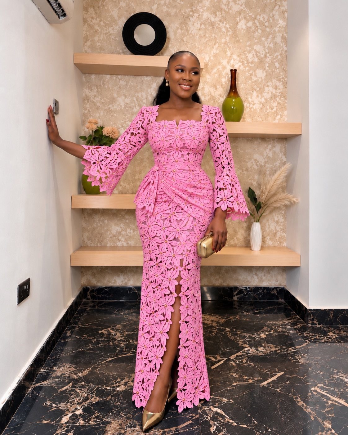 A woman wearing a long pink lace dress with bell sleeves and a front slit.