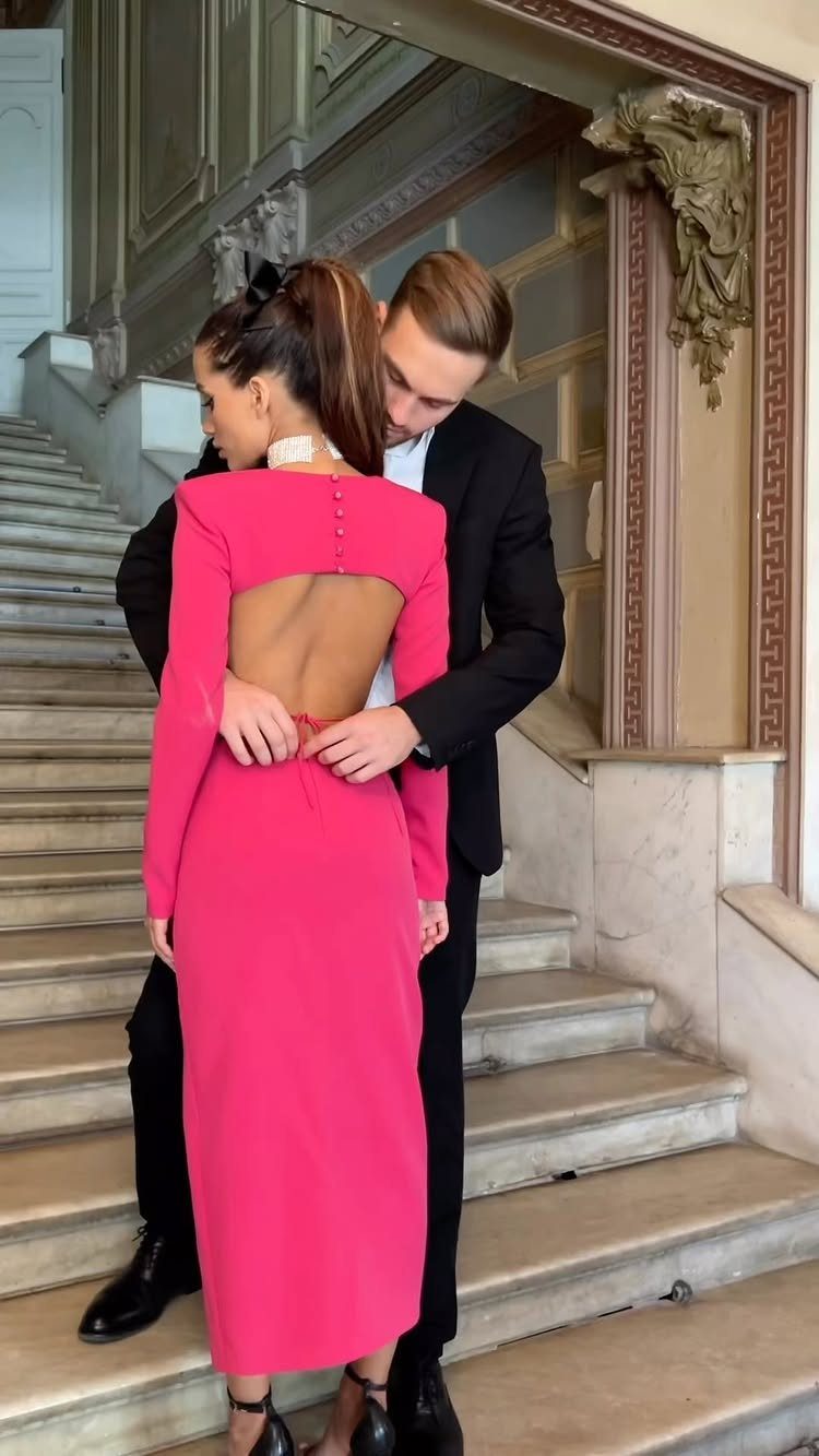 Woman in a long pink form-fitting dress standing on marble stairs with a man.