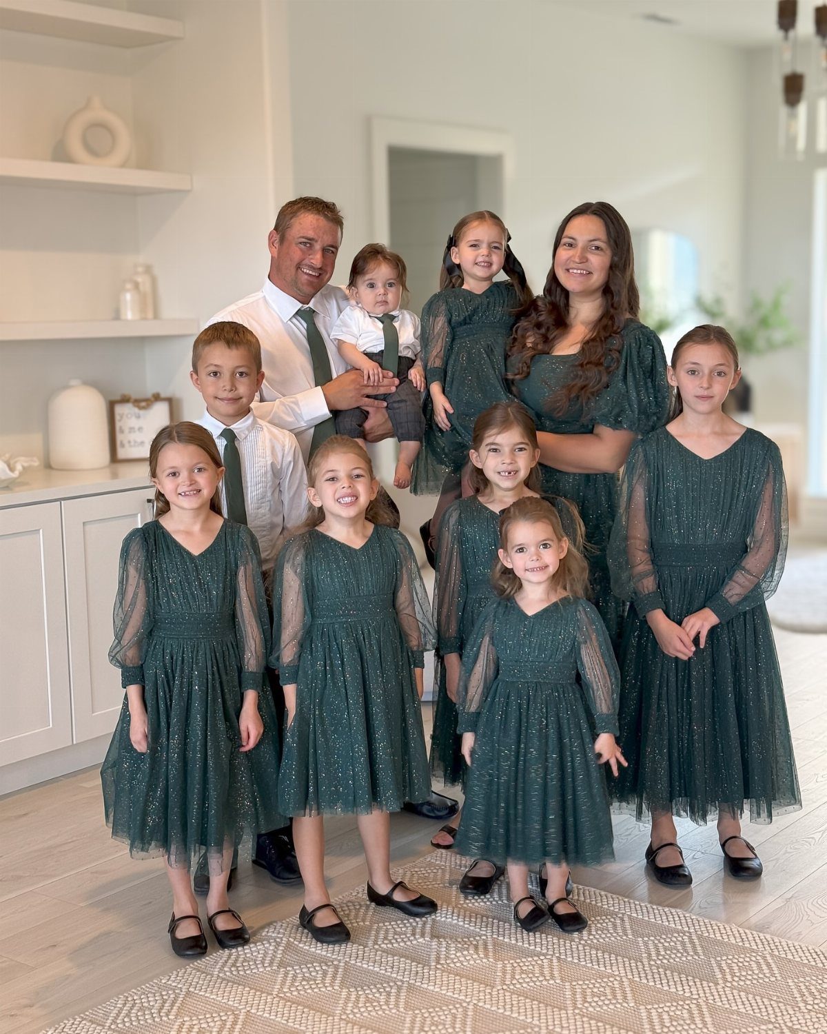 A large family posing together wearing coordinated white and dark green autumn outfits.