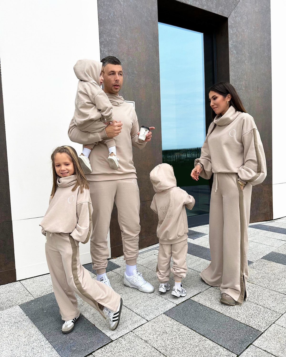 A family of five wearing matching beige comfortable loungewear sets standing outdoors.